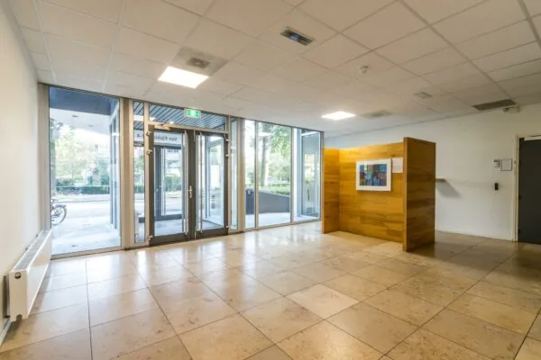 Moderne, lichte entreehal aan de Jan van Eycklaan met glazen deuren, een kunstwerk en houten wand.